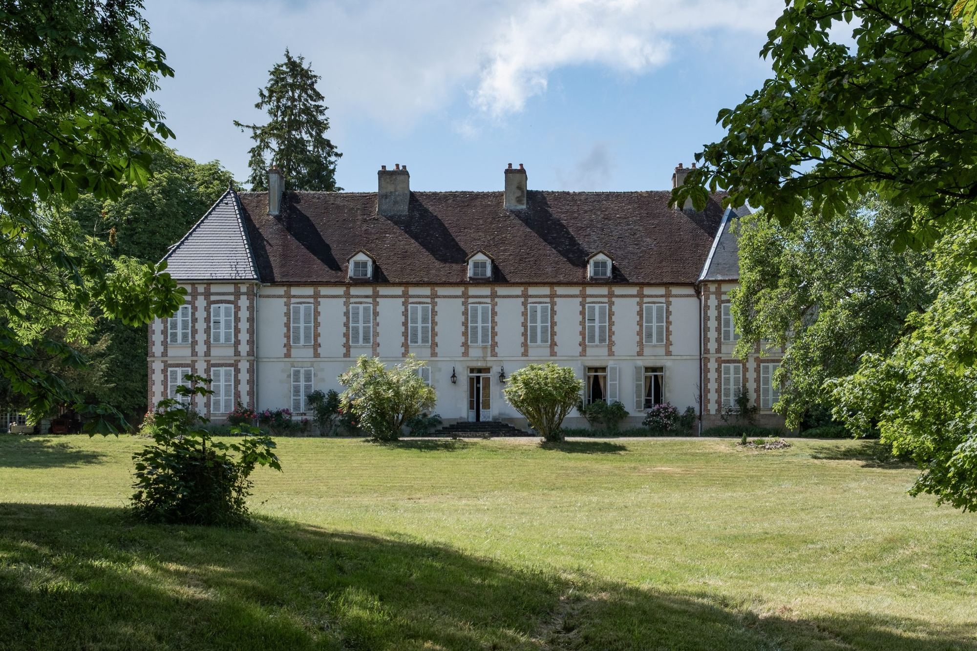 The facade of Château de Vindey across its lawn, framed by trees
