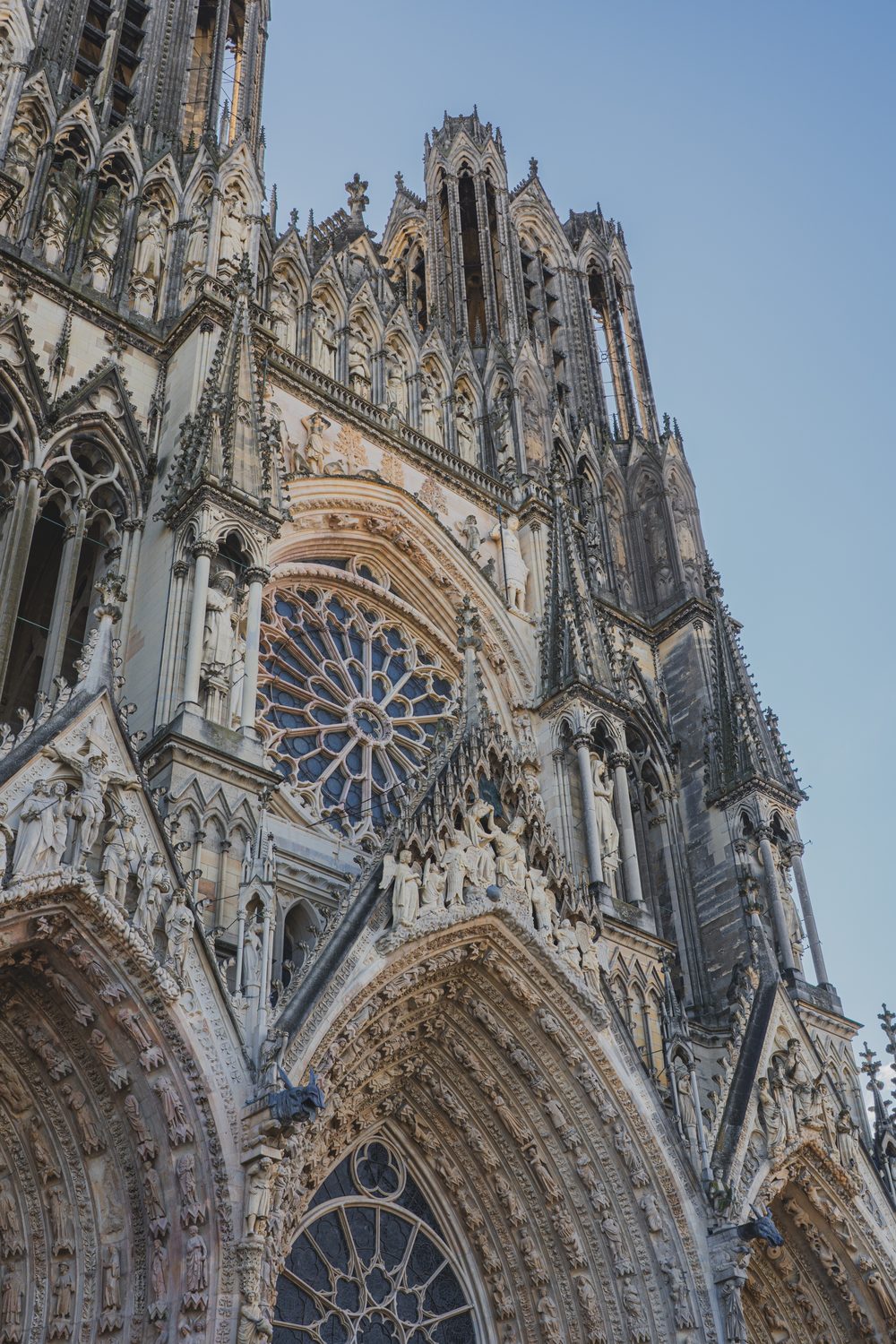 The Gothic west facade of Reims Cathedral with its rose window and sculpted portals against a clear sky